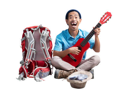 Asian man with a beanie hat and a backpack playing guitar to make money isolated over white...