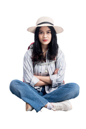 Asian woman with hat and backpack sitting with crossed arms isolated over white backgroundの写真素材