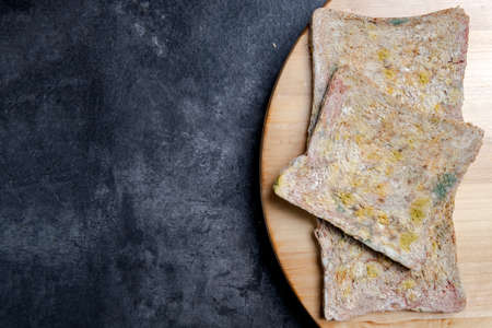Moldy slice of bread on the board with black background
