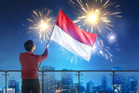 Rear view of Asian businessman holding an Indonesian flag with a night scene background. Indonesian...