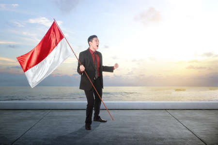 Asian businessman holding an Indonesian flag with a blue sky background. Indonesian independence dayの写真素材