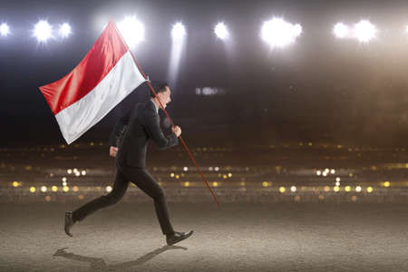 Asian businessman running while carrying an Indonesian flag with a spotlights background. Indonesian independence dayの写真素材