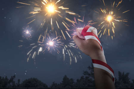 Human hand holding ribbon with the red and white color of the Indonesian flag with a fireworks background. Indonesian independence dayの写真素材