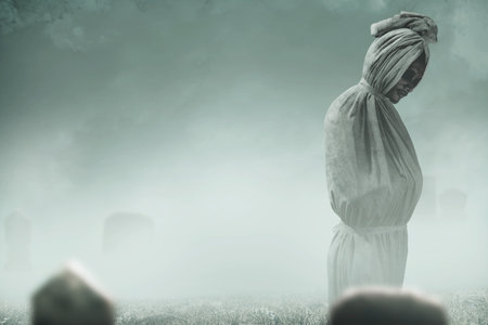 Pocong is covered with a white linen shroud standing in the cemetery. Halloween conceptの写真素材