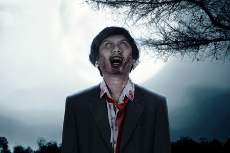 Scary zombie with blood and wound on his body standing with full moon backgroundの写真素材