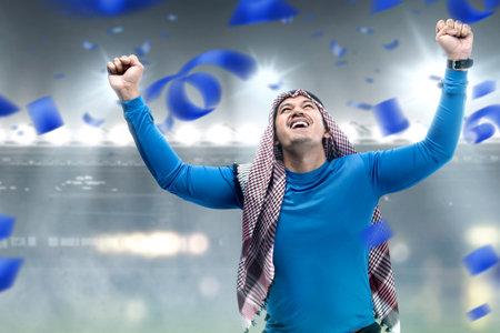 Asian man with keffiyeh standing with an excited expression on the football stadiumの写真素材
