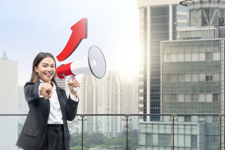 Asian businesswoman talking on a megaphone and pointing to you with a cityscapes backgroundの写真素材