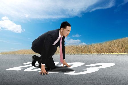 Asian businessman in start position ready to run on the street of 2023 with a blue sky background....