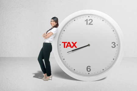 Asian businesswoman leaning on the clock with a countdown for taxes on white backgroundの写真素材
