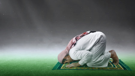 Muslim man with keffiyeh and agal in praying position (salat) on the prayer rug with light backgroundの写真素材