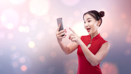 Asian Chinese woman in a cheongsam dress using a mobile phone. Happy Chinese New Yearの写真素材