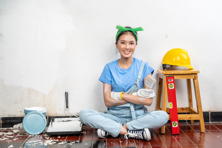 Asian young housewife in a glove holding a paintbrush with white wall background