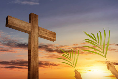 Cross and palm leaf on the field with a sunset sky background. Palm Sunday Concept