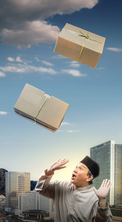 Asian Muslim man afraid of dropping box with blue sky background