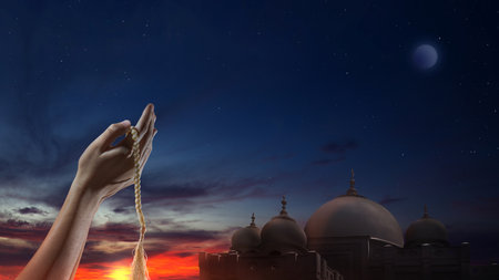 Muslim man praying with prayer beads in his hands with mosque backgroundの写真素材
