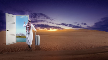 Rear view of an Arab man wearing keffiyeh holding a mobile phone with a suitcase walking inside the doorの写真素材