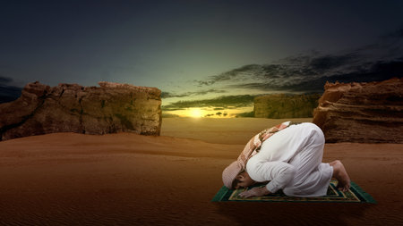 Muslim man with keffiyeh and agal in praying position (salat) on the prayer rug in the desertの写真素材