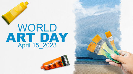 A human hand with a paintbrush draws a landscape on a white canvas. World Art Day conceptの写真素材