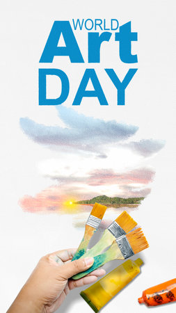A human hand with a paintbrush draws a landscape on a white canvas. World Art Day conceptの写真素材