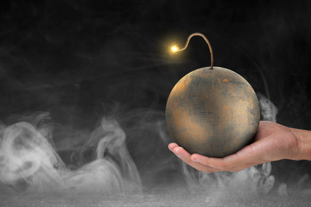 A human hand holding a ball bomb with a burning fuse on dark backgroundの写真素材