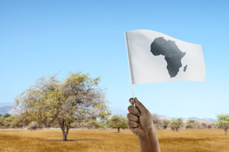 A human hand holding a Flag with African maps with a blue sky background. Africa day conceptの写真素材