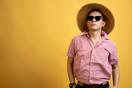 Man with a shirt wearing sunglasses and a hat standing on a colored backgroundの写真素材