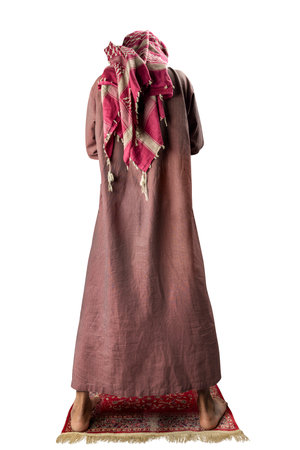 Muslim man with a beard wearing keffiyeh with agal in praying position (salat) on the prayer rug...