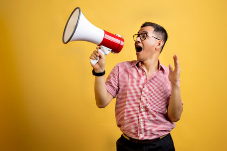 Man with eyeglasses and a shirt talking on a megaphone on a colored backgroundの写真素材