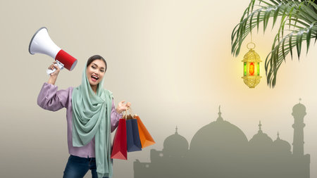Asian Muslim woman in a headscarf holding a megaphone and shopping bags on a colored backgroundの写真素材