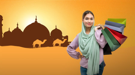 Asian Muslim woman in a headscarf holding shopping bags on a colored backgroundの写真素材