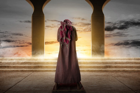 Muslim man with a beard wearing keffiyeh with agal in praying position (salat) on the prayer rug with the sunset scene backgroundの写真素材