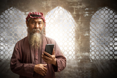 Muslim man with a beard wearing keffiyeh with agal using mobile phone with the blue sky backgroundの写真素材