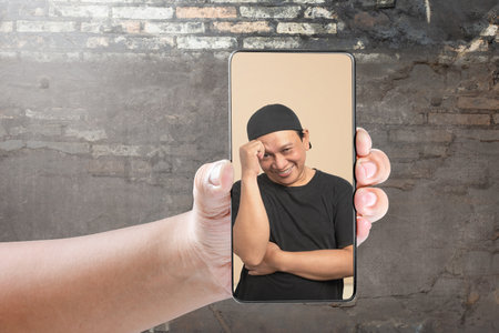 Portrait of an Asian man with a thinking facial expression on the mobile phone screen. Meme face conceptの写真素材