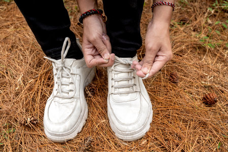 Women's legs tie her shoelace while trekking in the forest. Traveling activity