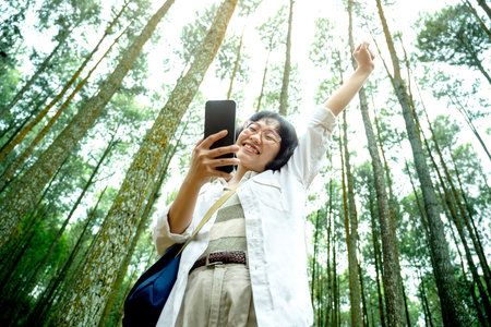 Asian woman using a mobile phone with a happy expression in the forest. Traveling activityの写真素材