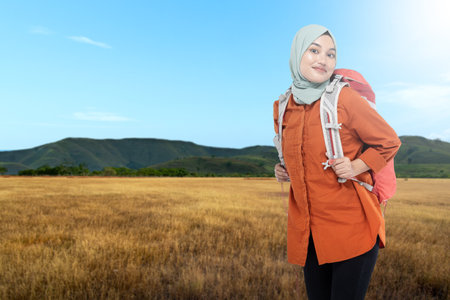 Asian Muslim woman in a headscarf carrying a backpack on the meadow with a blue sky background. World tourism day conceptの写真素材