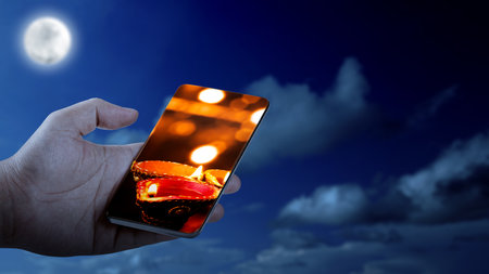 Human hand showing Diya oil lamps for the Diwali festival on the mobile phone screen. Diwali...