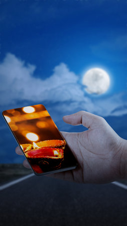 Human hand showing Diya oil lamps for the Diwali festival on the mobile phone screen. Diwali Festival. The Hindu Festival of Lights celebrationの写真素材