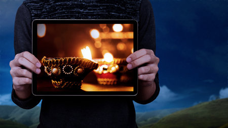 Human hand showing Diya oil lamps for the Diwali festival on the tablet screen. Diwali Festival. The...
