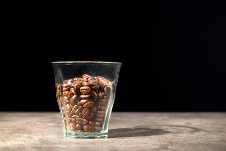 Glass with coffee beans on the table with a black backgroundの写真素材