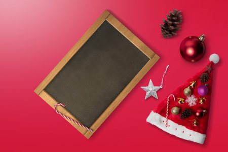 Santa Claus hat with Christmas ornament with empty chalkboard on a colored background. Christmas decoration concept. Empty chalkboard for copy spaceの写真素材