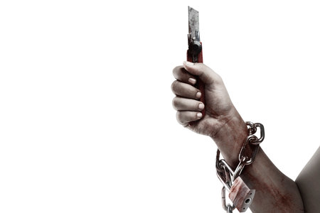 The hand of a scary zombie with blood and wounds holding a knife while tied to the iron chain is...