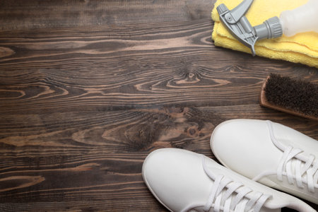 Brush, microfiber cloth, and bottle sprayer with white sneakers on a wooden background. Shoe care conceptの写真素材