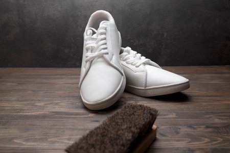 Brush with white sneakers on a wooden background. Shoe care conceptの写真素材