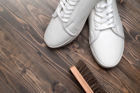 Brush with white sneakers on a wooden background. Shoe care conceptの写真素材