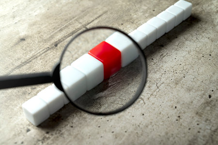 Magnifying glass focuses on a row of small cubes on a wooden tableの写真素材