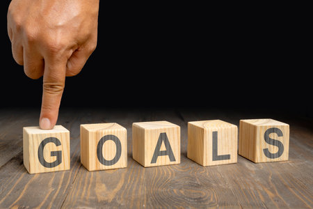 A human hand shows a row of wooden cubes with GOALS letters on a wooden table. Concept of planning for successの写真素材