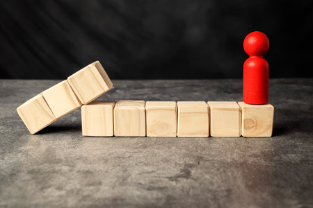 A wooden figure and a row of wooden cubes on a wooden tableの写真素材