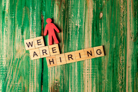 Wooden figure and wooden cubes with We Are Hiring letters on a wooden background. Human resources...