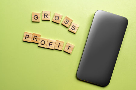 Closeup view of a mobile phone with a blank screen and a wooden cube with a Gross Profit letter. Financial conceptの写真素材